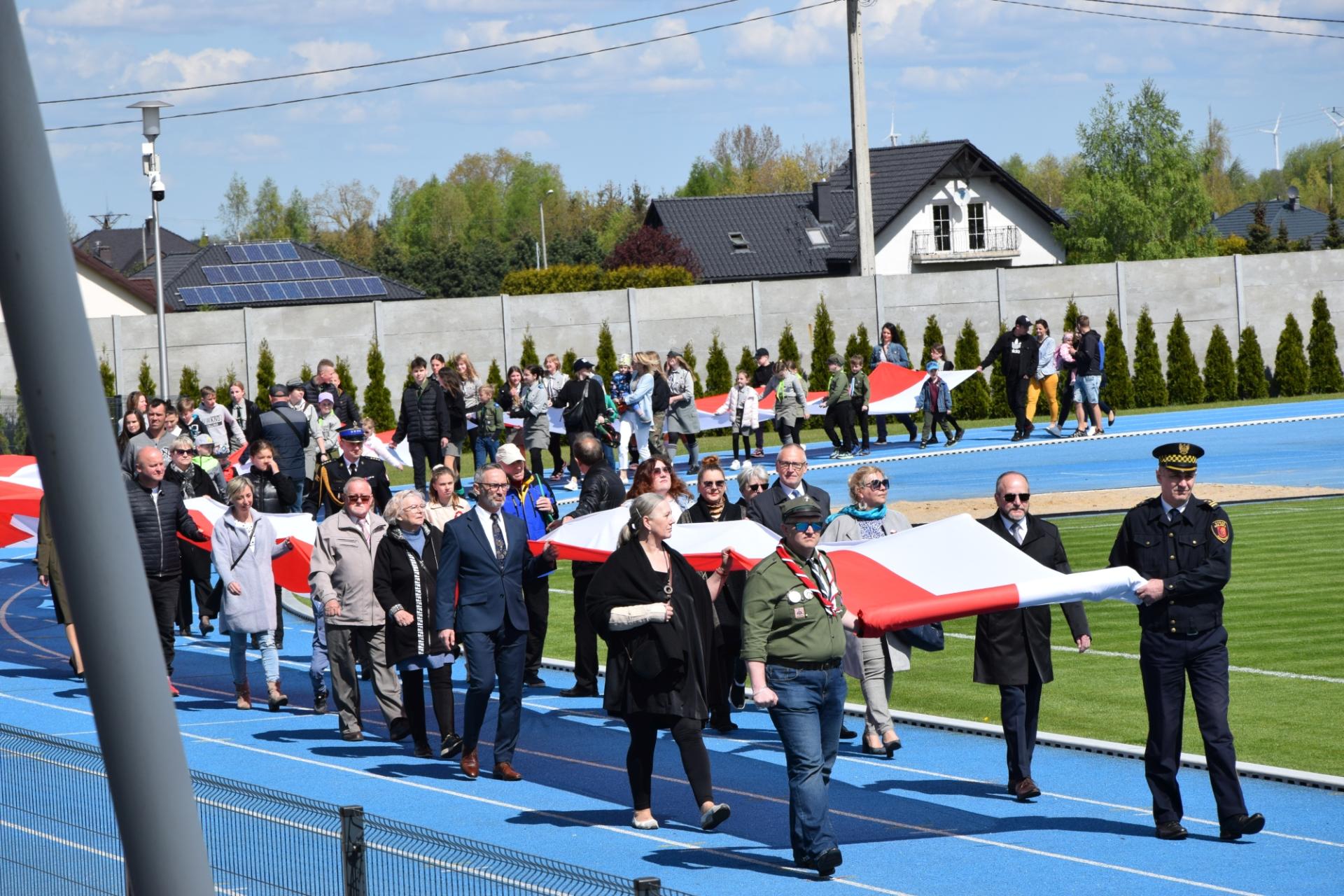 Tłum ludzi niosących długą flagę Polski na stadionie miejskim
